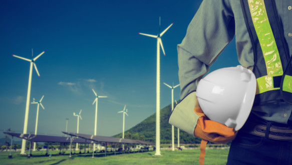 Environmental engineer standing in front of a dozen wind mills while holding his hard hat